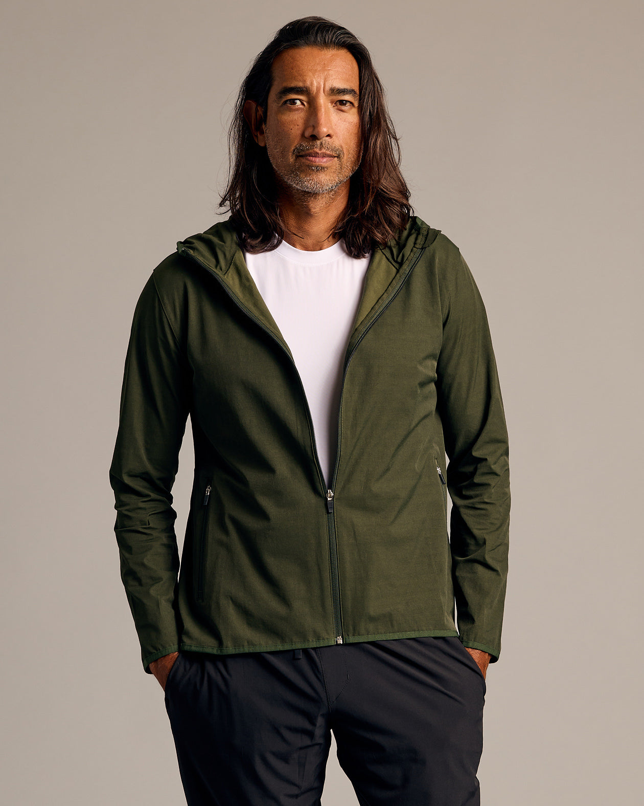 Olive Tech Windbreaker on man, hands in pockets, studio setting.