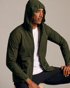 Olive Tech Windbreaker on seated man, hood up, casual pose.
