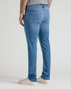 True ClassicRear view of a person wearing slim-fit blue jeans with white sneakers against a plain light gray studio background.
