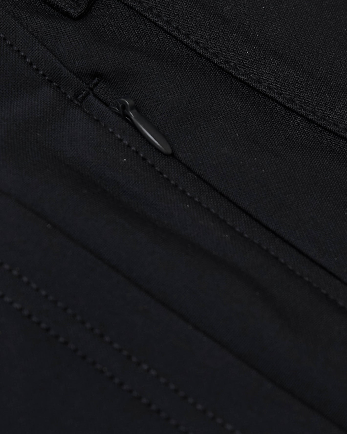 Black Commuter Short fabric close-up with stitching and zipper pull.