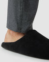 Foot slipping into Black Slippers with dark gray lounge pants visible.