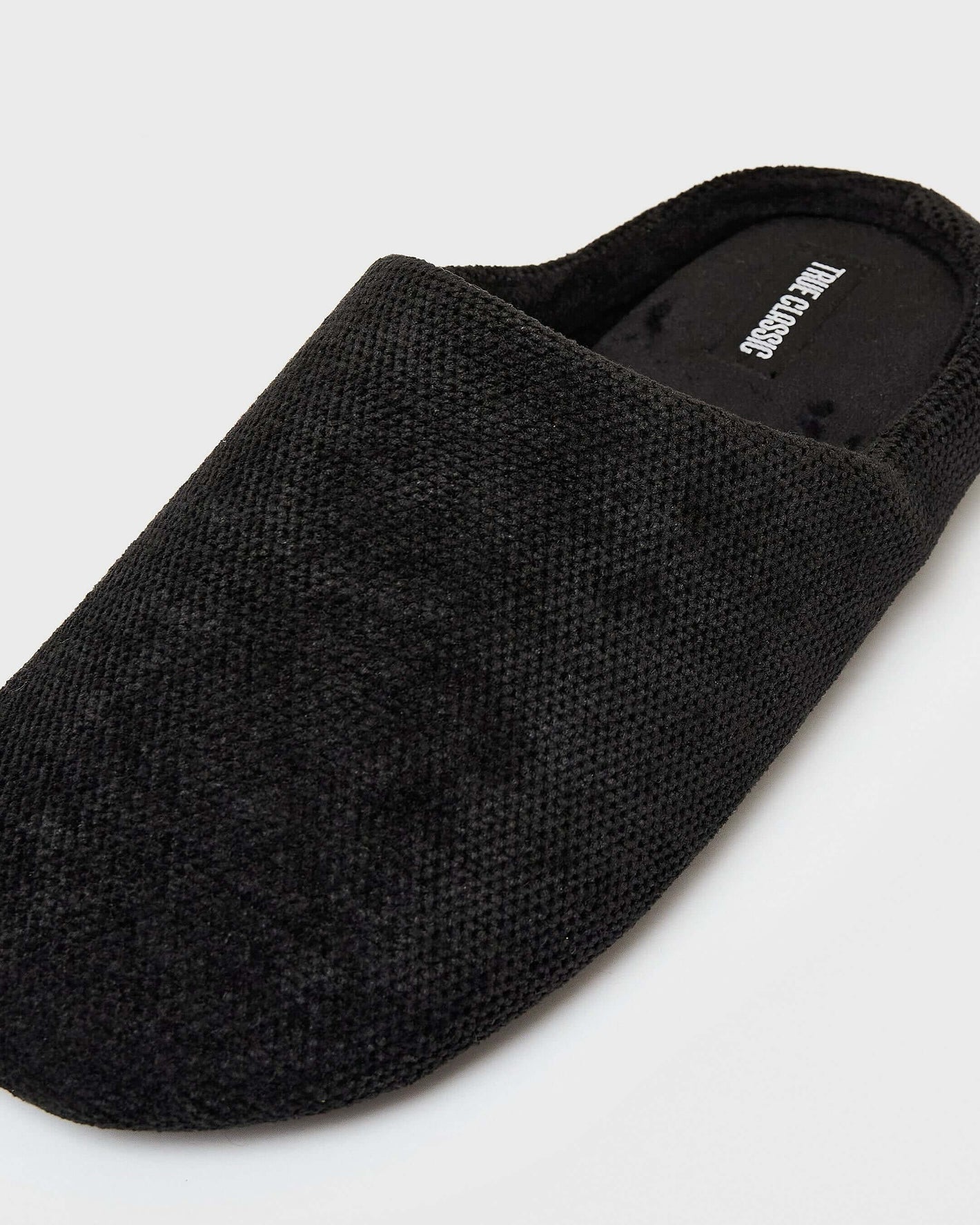 Black Slippers: Close-up of a textured knit slip-on with open back and rounded toe.