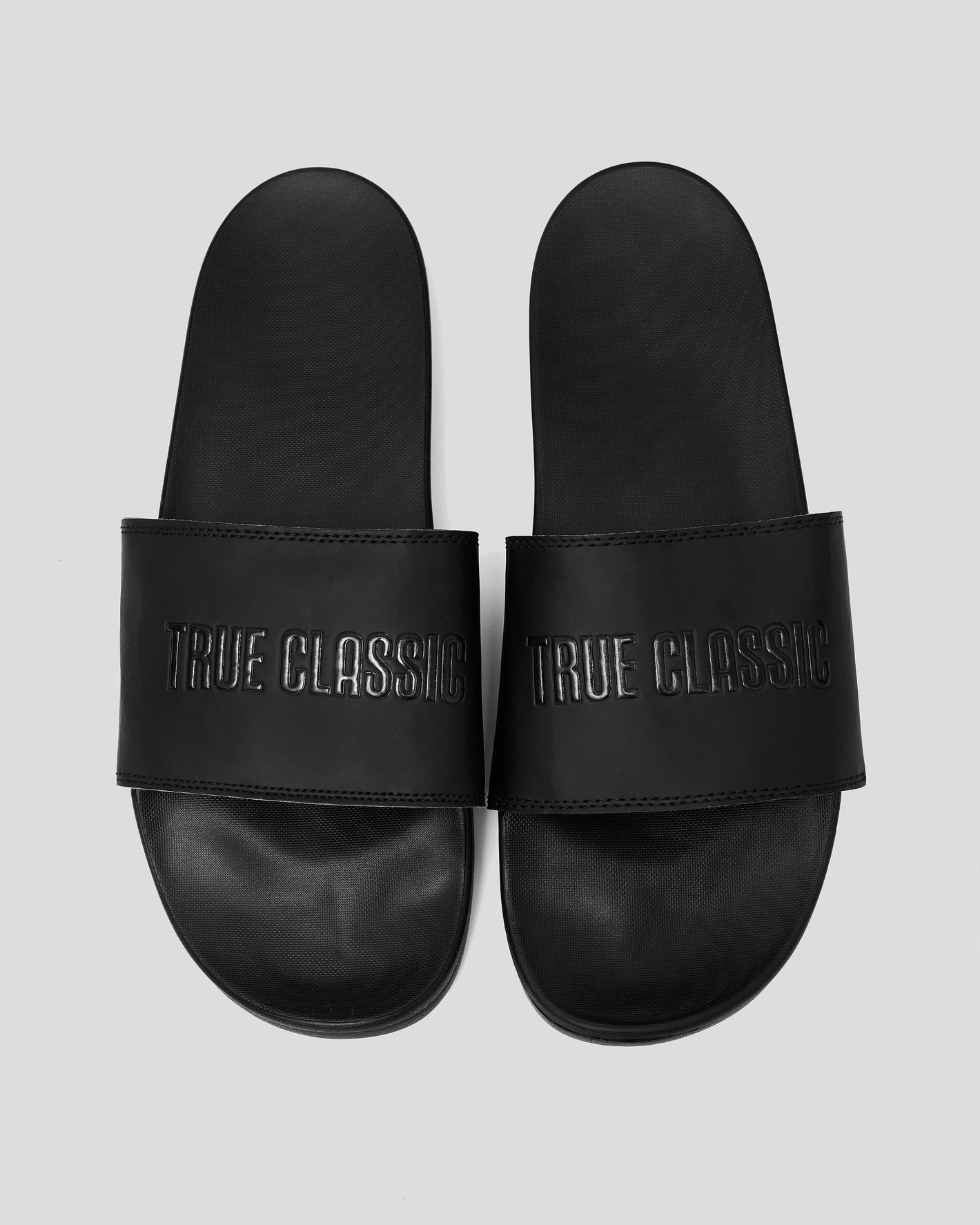 Black Comfort Slides with TRUE CLASSIC embossed strap, side by side.