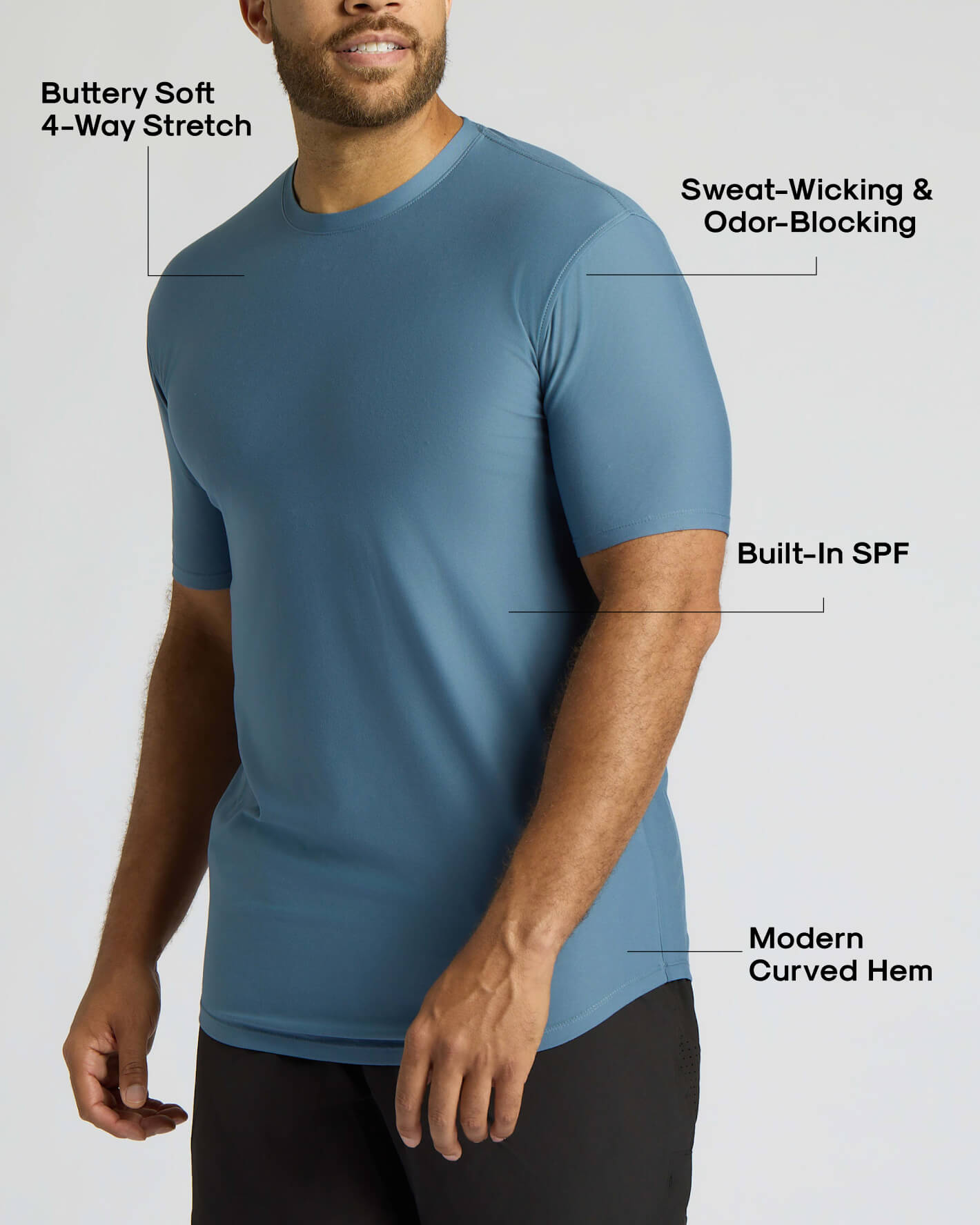 A man wearing a blue short-sleeve athletic shirt with text callouts highlighting features such as buttery soft 4-way stretch, sweat-wicking and odor-blocking, built-in SPF, and a modern curved hem.
