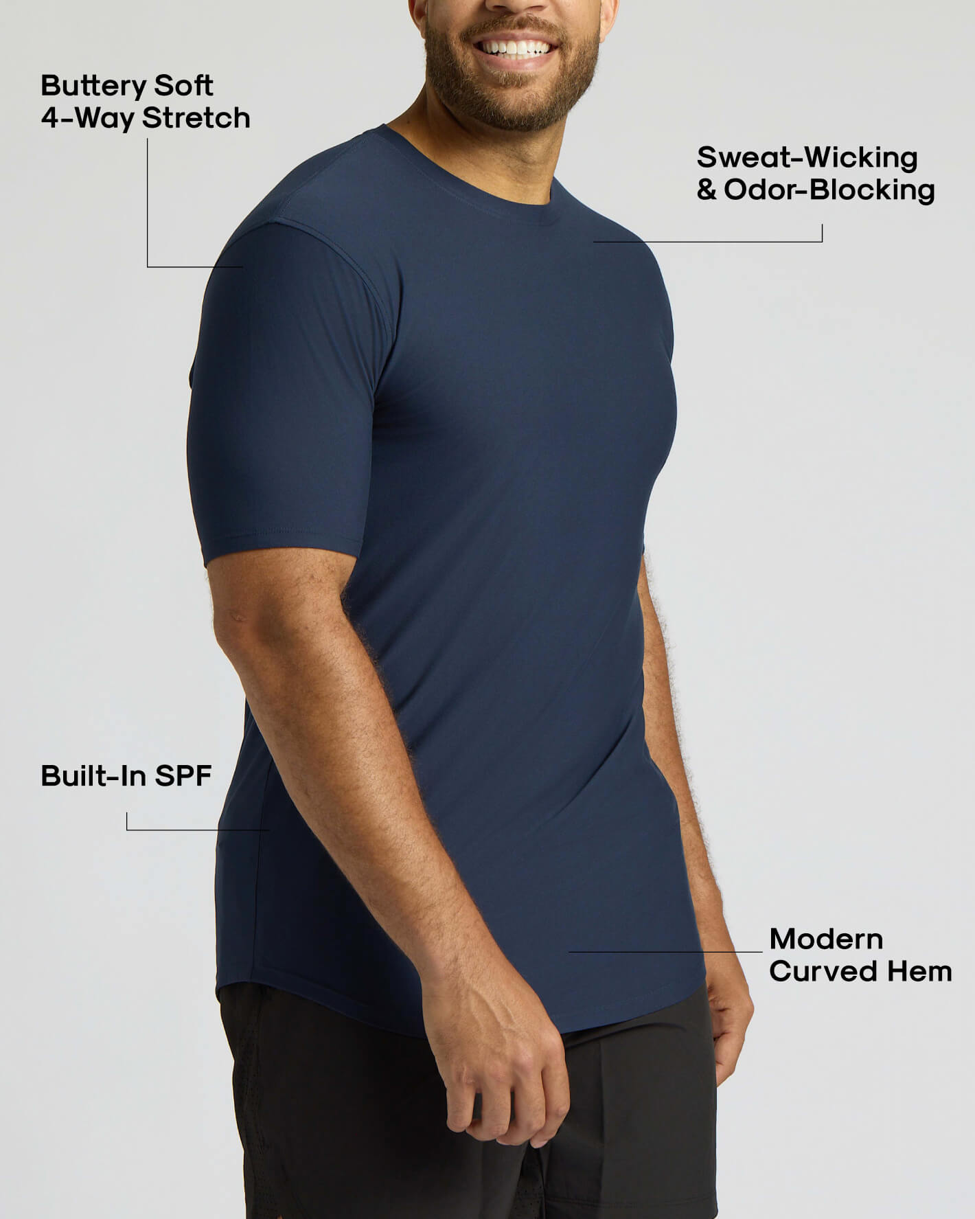 A man wearing a navy blue short-sleeve athletic t-shirt, shown from the chest down against a light gray background, with text callouts highlighting features like 4-way stretch, sweat-wicking, built-in SPF, and modern curved hem.
