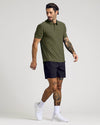 Man with tattoos wearing a Dark Heather Pear Active Polo 2.0 paired with black shorts and white sneakers, posing against a plain light background.