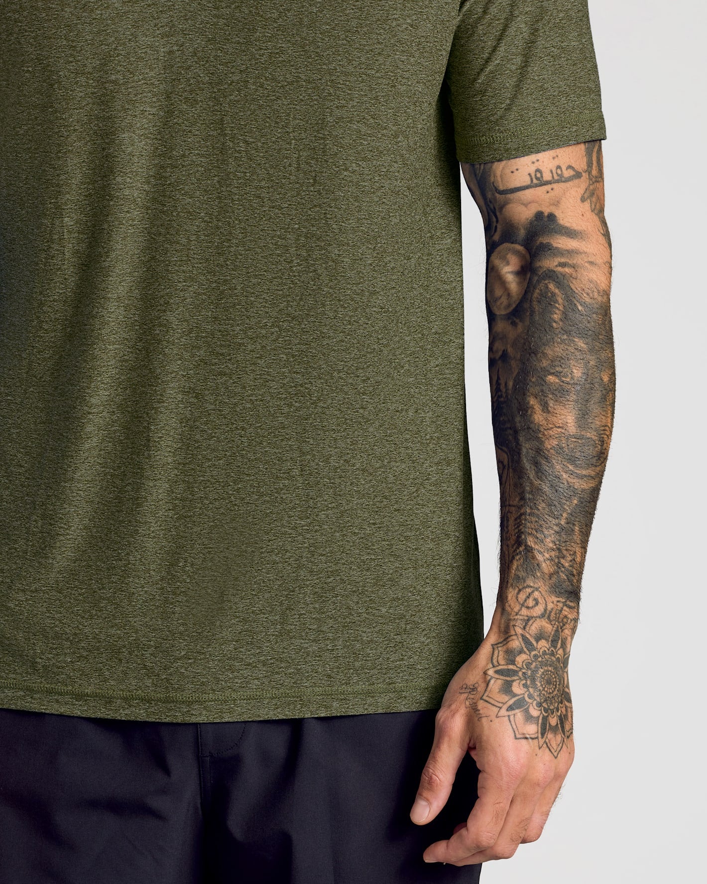 Close-up of a man wearing a Dark Heather Pear Active Polo 2.0 in olive green with visible tattoos on his arm, showcasing the soft, breathable fabric of this men's basics polo shirt.