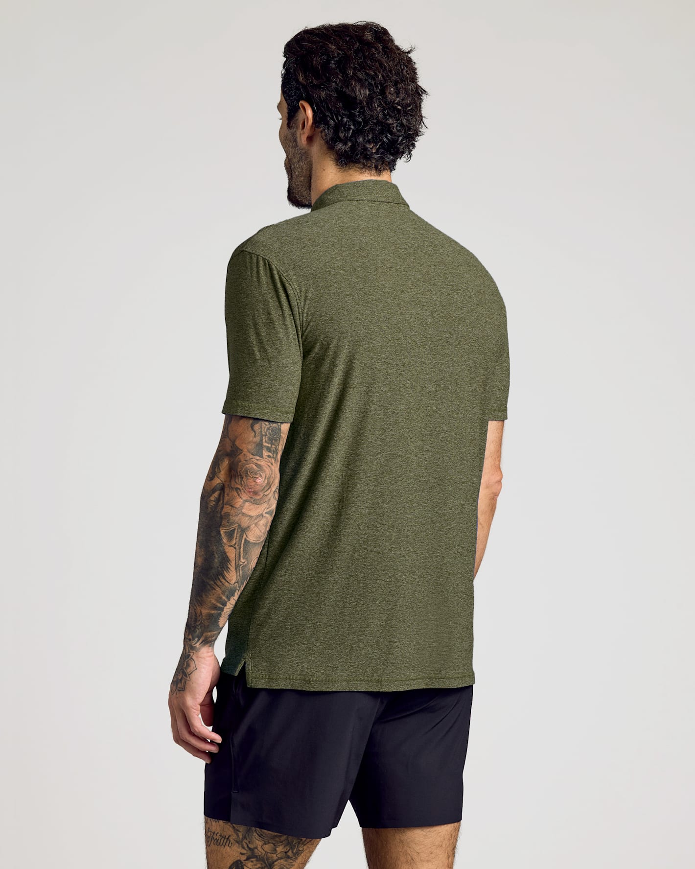 Man wearing a Dark Heather Pear Active Polo 2.0 with short sleeves, shown from the back, paired with black athletic shorts in a neutral studio setting.