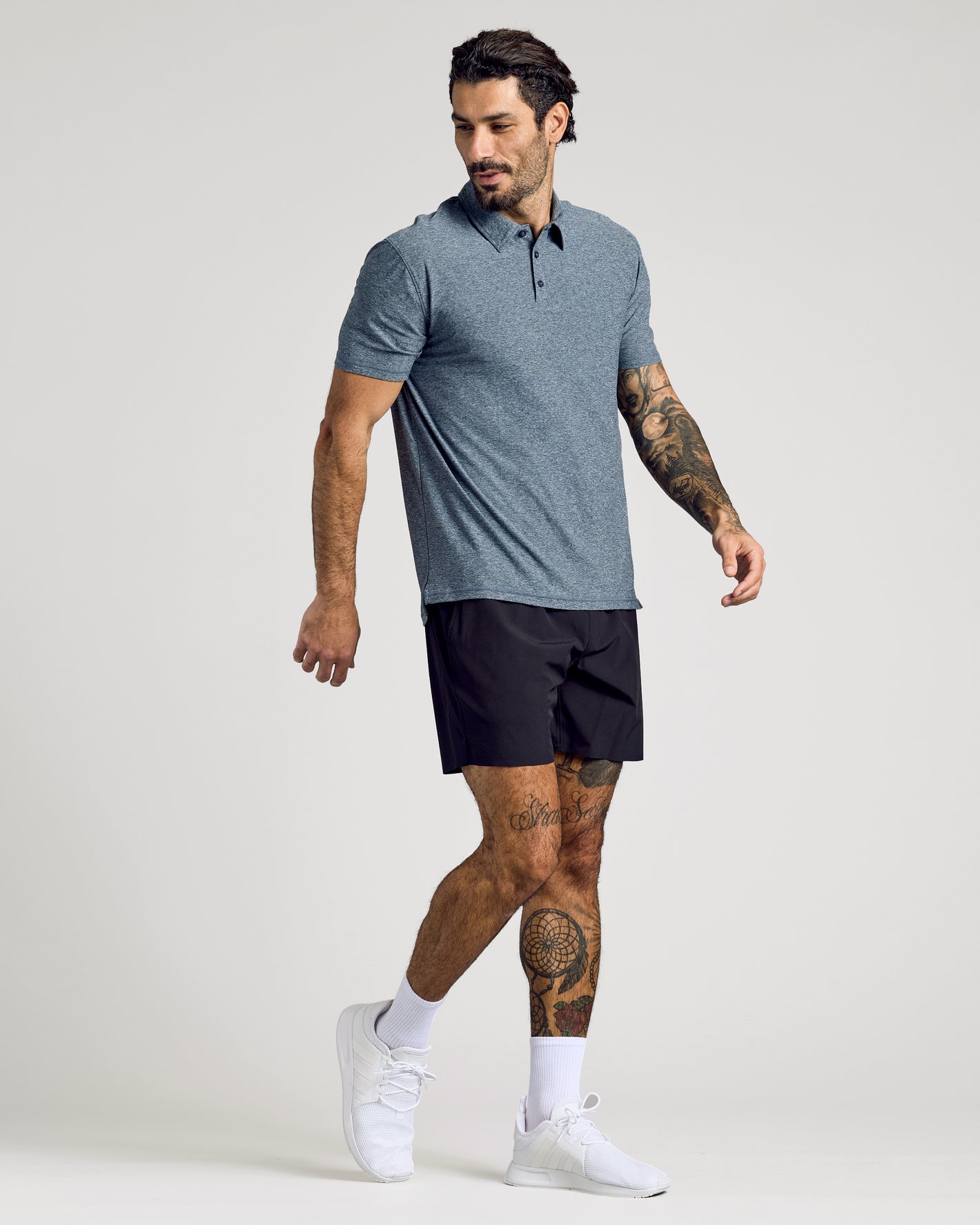 Man wearing Heather Navy Active Short Sleeve Polo with black shorts and white sneakers.