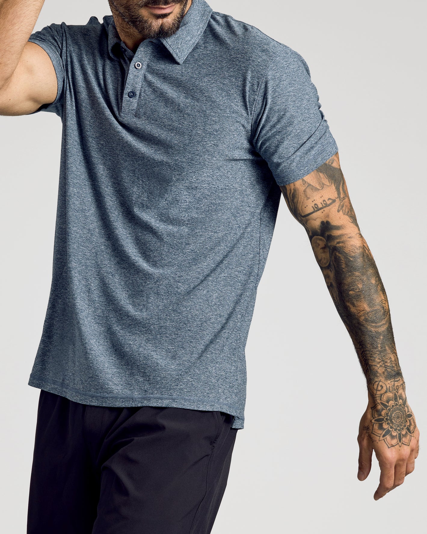 Man wearing Heather Navy Active Short Sleeve Polo, showcasing tattooed arm.