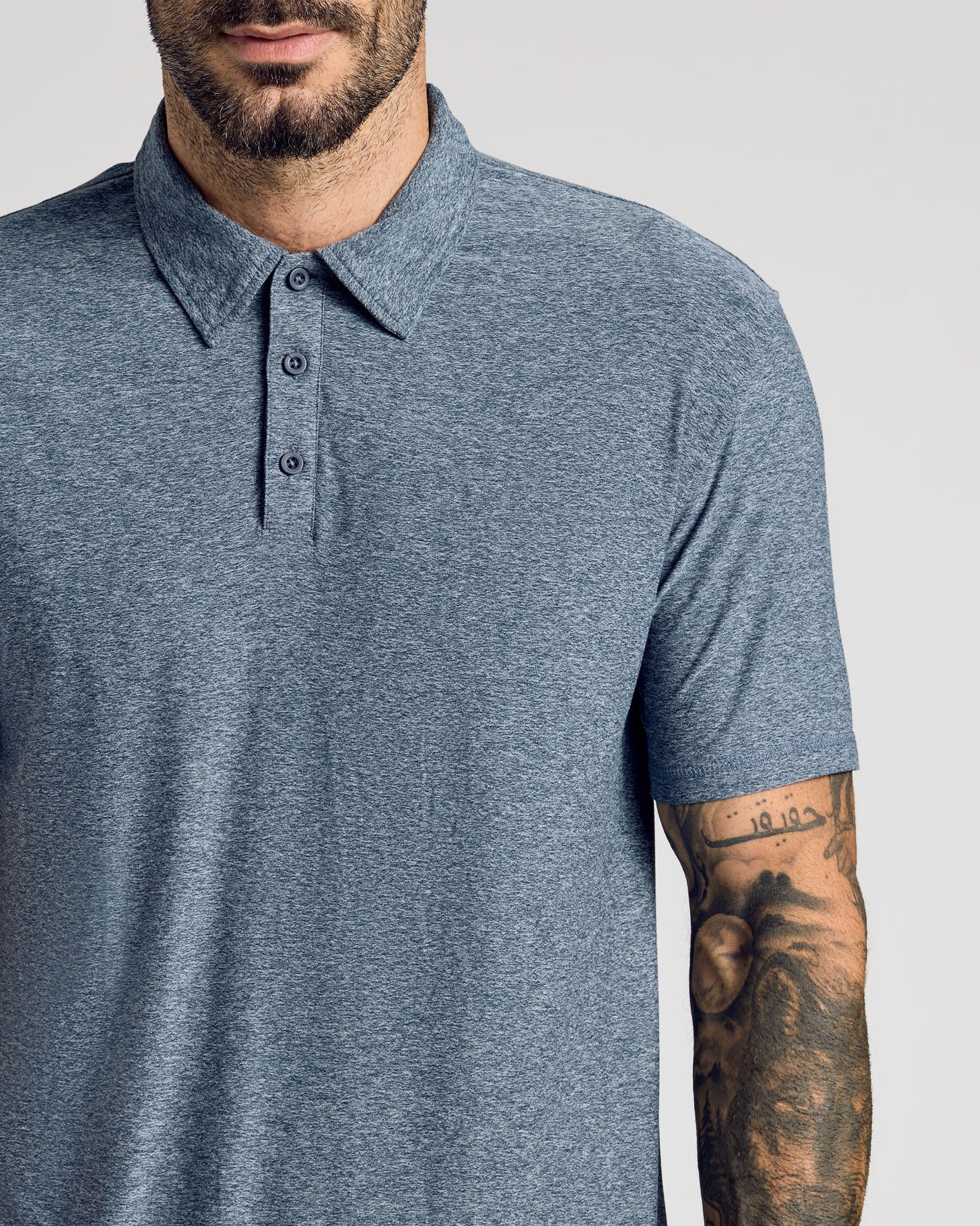 Man wearing Heather Navy Active Short Sleeve Polo, tattooed forearm visible.
