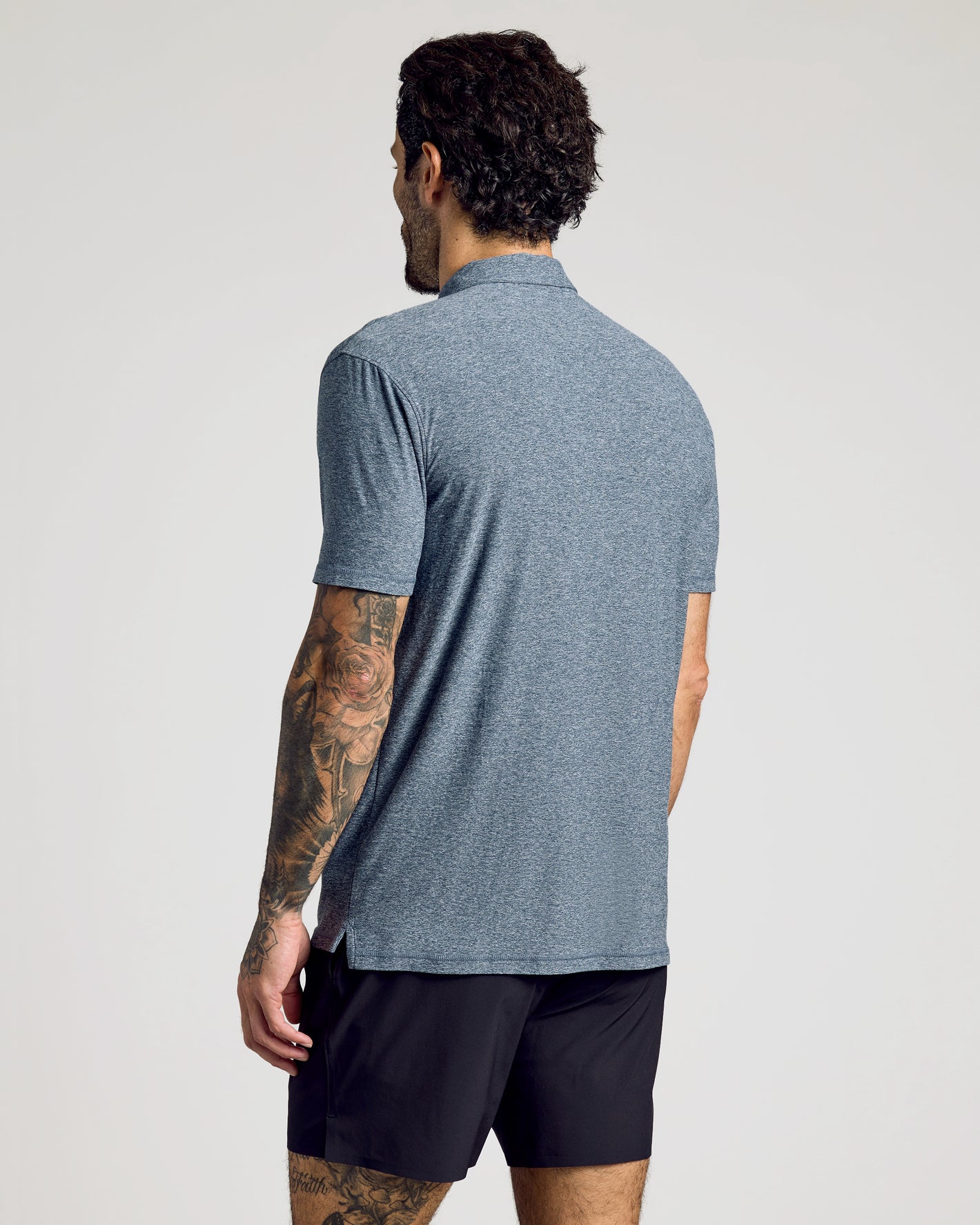 Man wearing Heather Navy Active Short Sleeve Polo, showcasing back view and tattoos.
