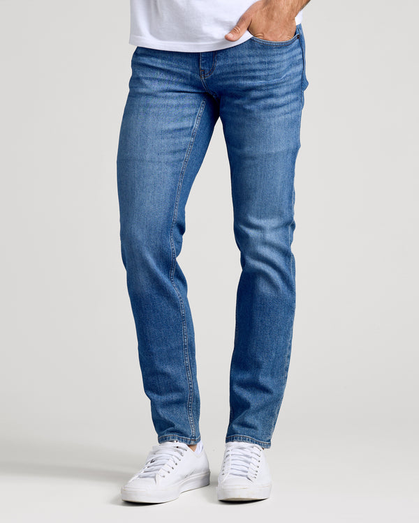 Model in Medium Indigo Wash Slim Authentic Denim Jeans and white sneakers.