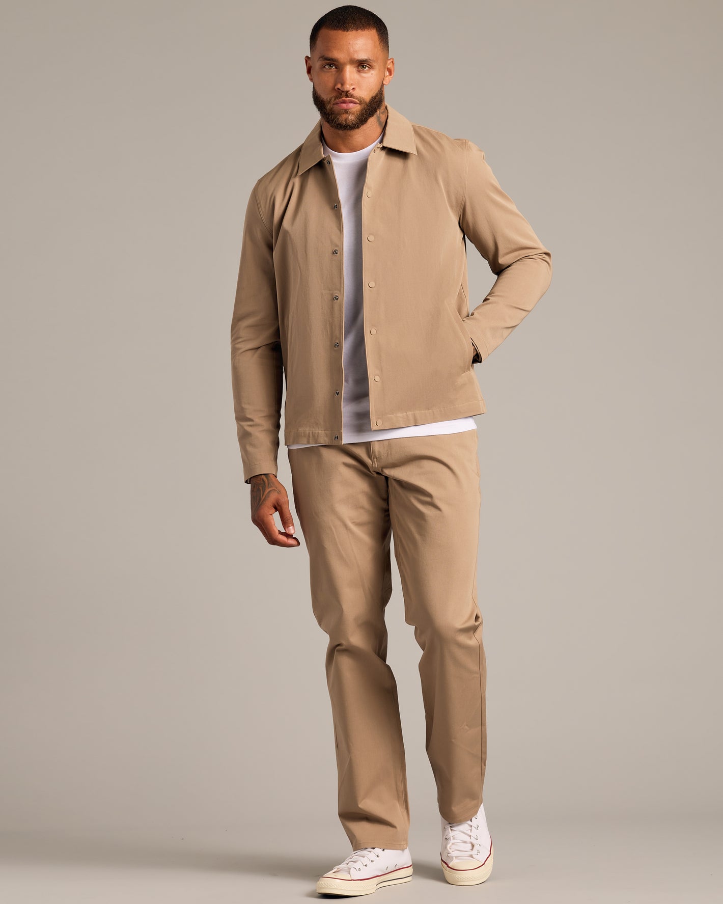 Model in Khaki Coaches Jacket, white tee, matching trousers, sneakers.