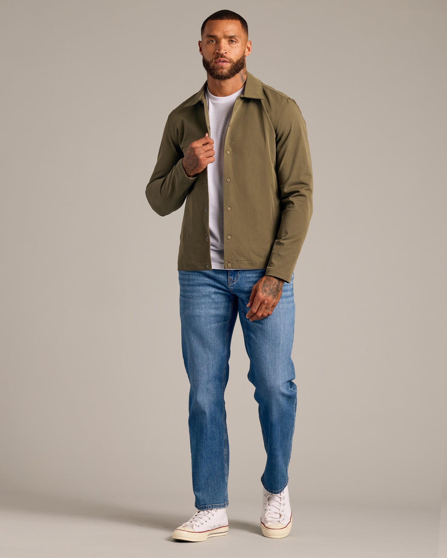 Man in Military Green Coaches Jacket with jeans and sneakers.