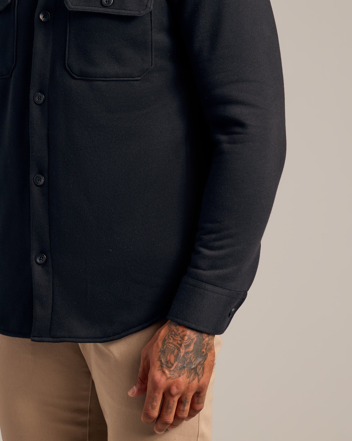 Black Fleece Shirt Jacket with chest flap pockets and tattooed hand visible.