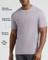 A man wearing a light lavender-gray short-sleeve crewneck t-shirt, with text callouts highlighting features like durability, arm fit, torso roominess, and smooth feel.