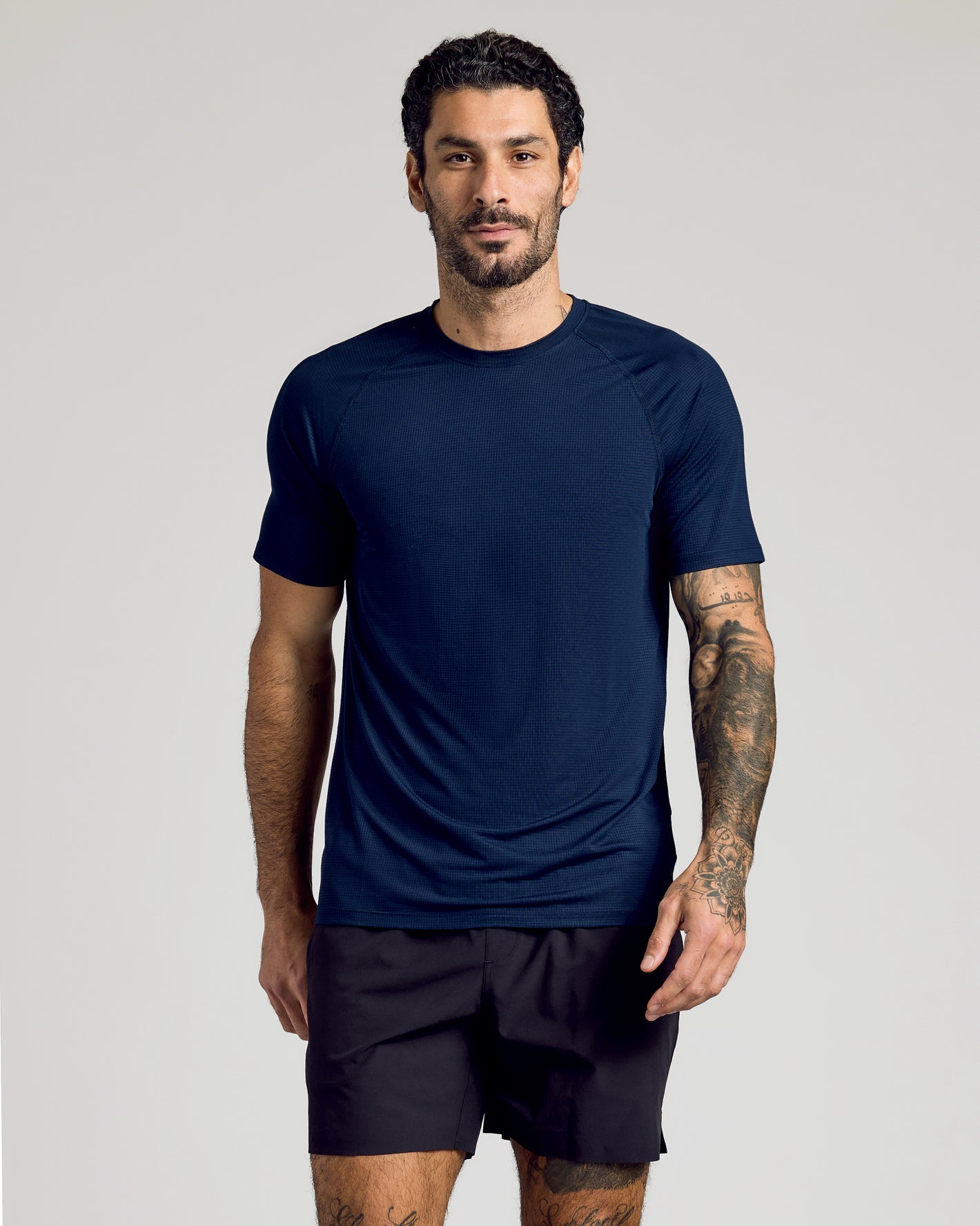 Man wearing Navy Active Mesh Raglan Tee, showcasing tattoos and relaxed stance.