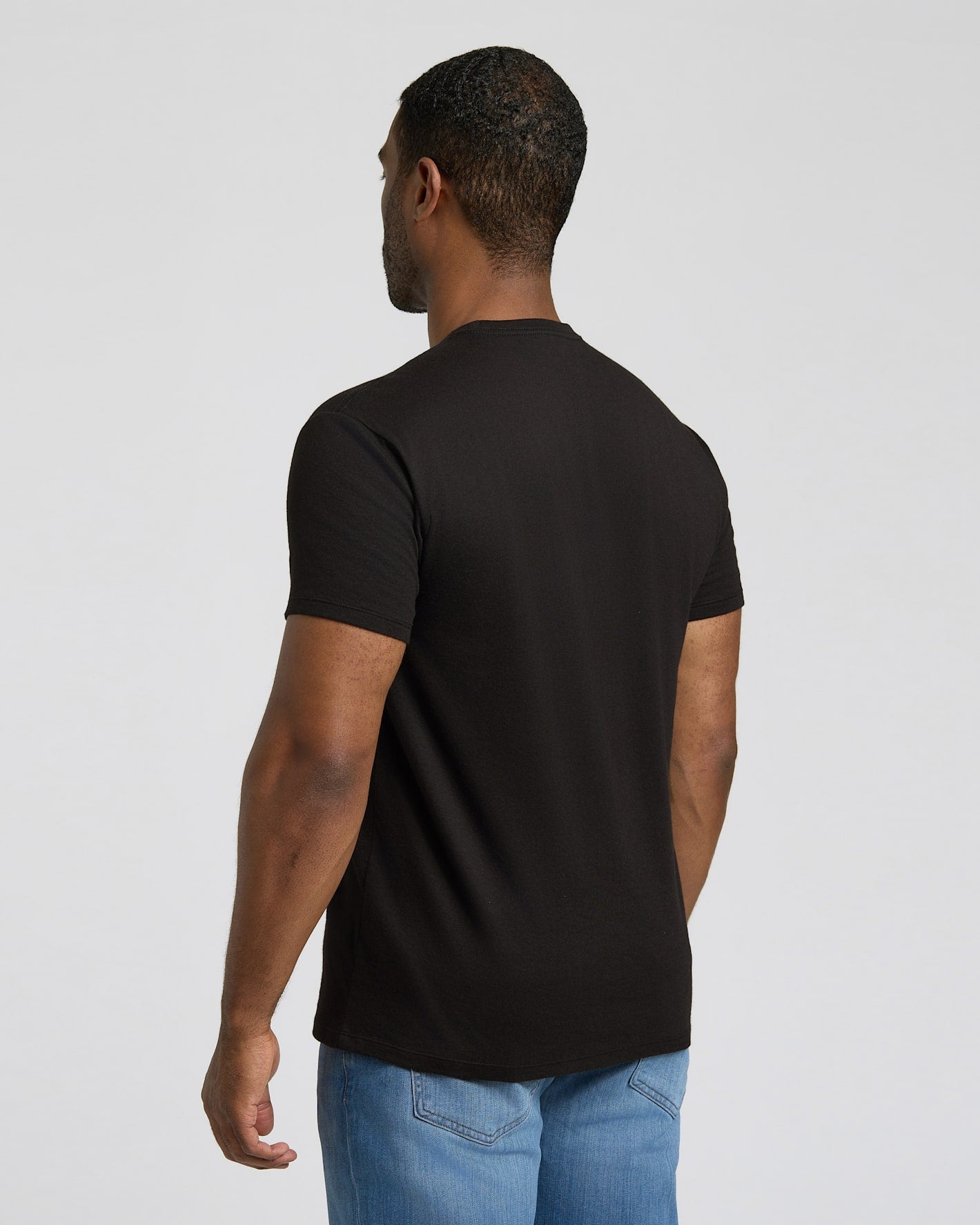 Man wearing a black t-shirt and blue jeans on a light gray background