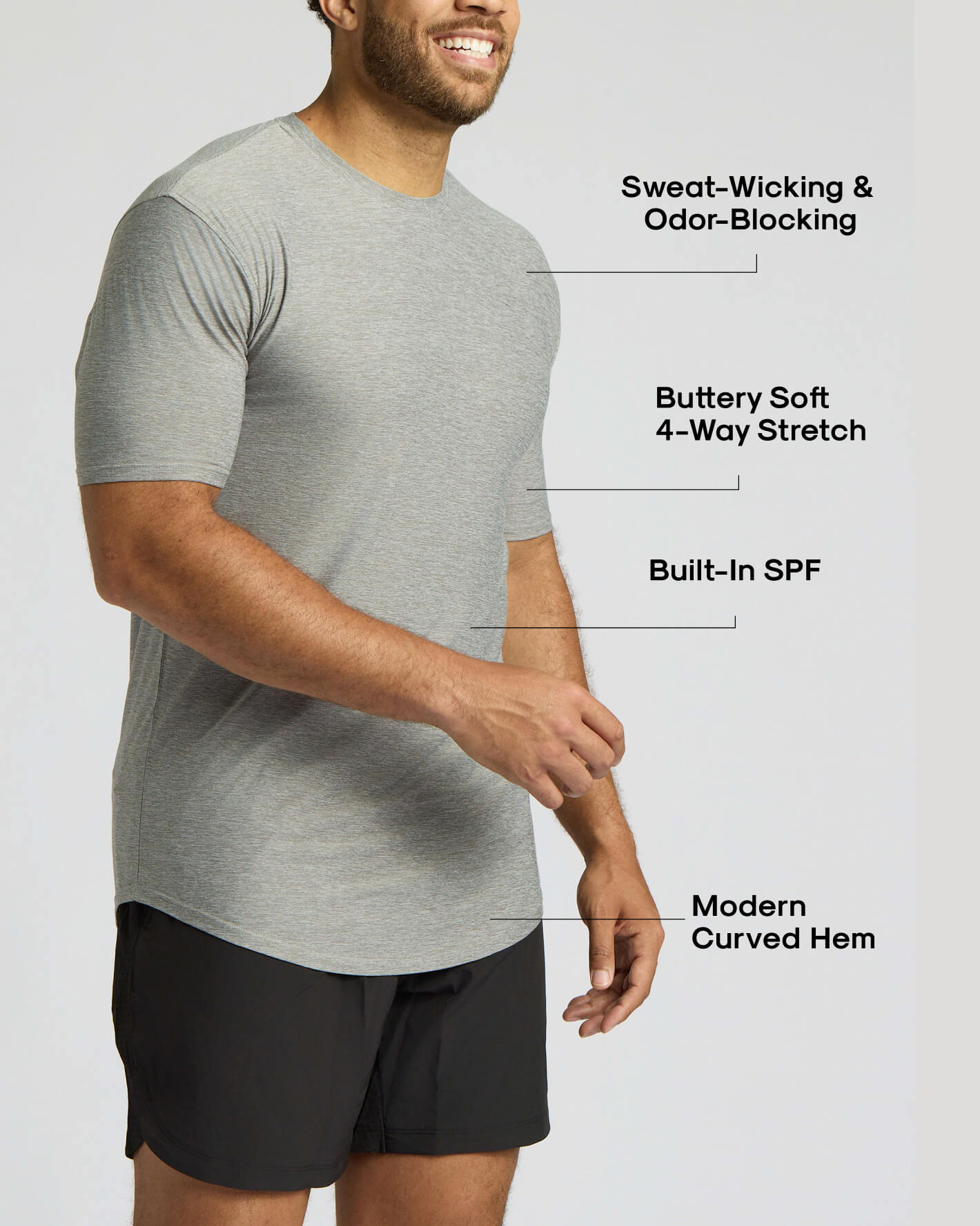 A man wearing a light heather gray short-sleeve athletic t-shirt with black shorts, shown against a light gray background with text callouts highlighting features like sweat-wicking, odor-blocking, stretch, built-in SPF, and curved hem.