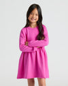 Girl in pink Girls Long Sleeve Fleece Dress, arms crossed, smiling.
