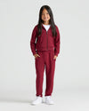 Girl in burgundy tracksuit from Girls Deep Emerald & Dark Maroon Cropped Zip Hoodie 2-Pack.