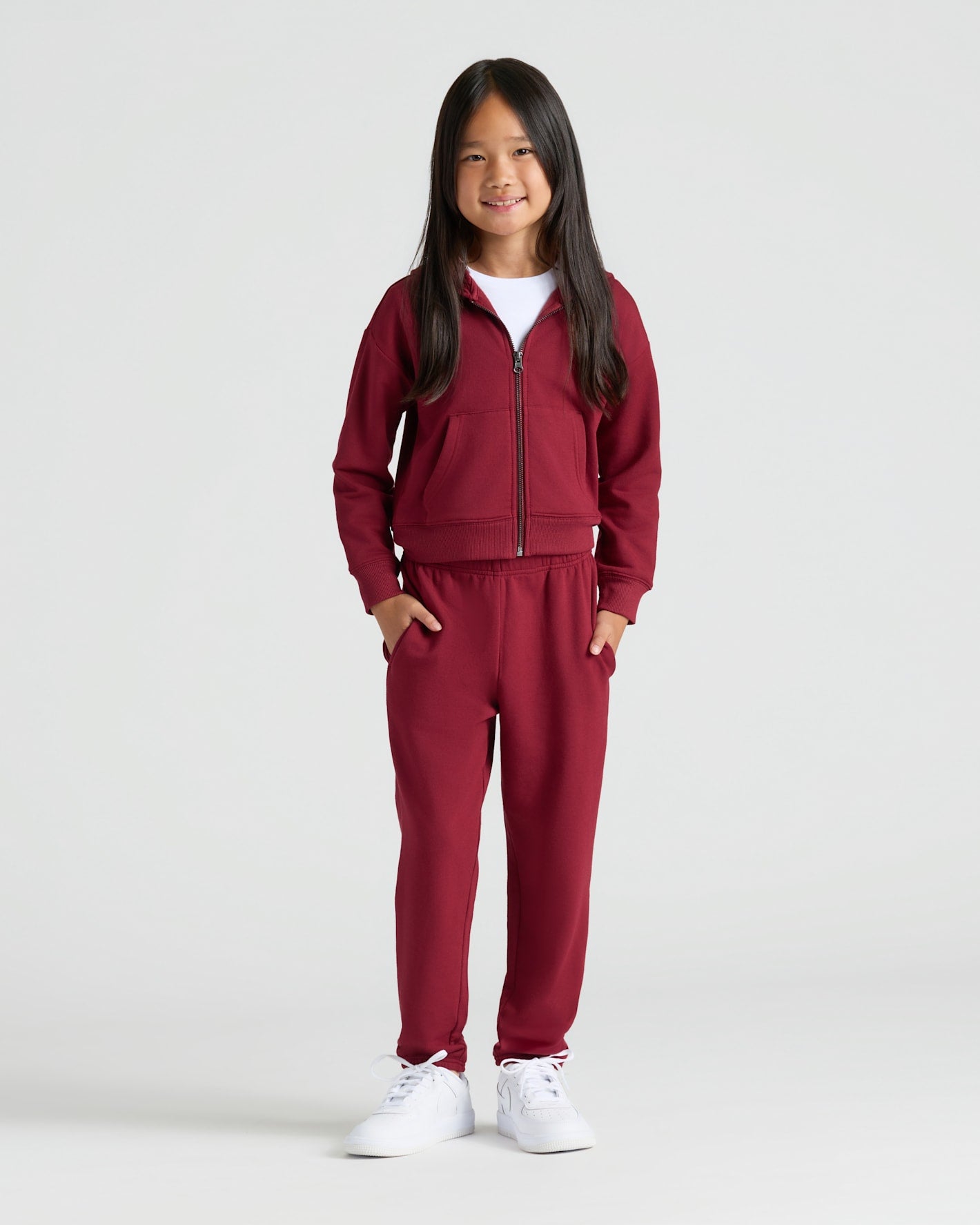 Girl in burgundy tracksuit from Girls Deep Emerald & Dark Maroon Cropped Zip Hoodie 2-Pack.
