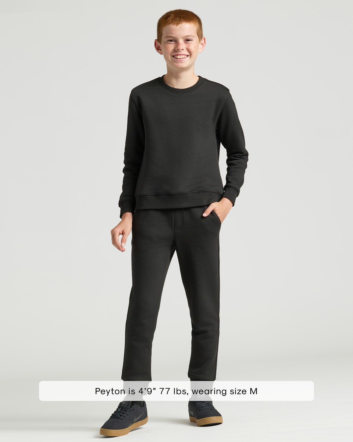 Boy in Boys' Black Fleece Jogger, smiling, with matching sweatshirt and sneakers.