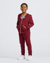 Boy in Boys' Dark Maroon Fleece Jogger, smiling with hands in pockets.