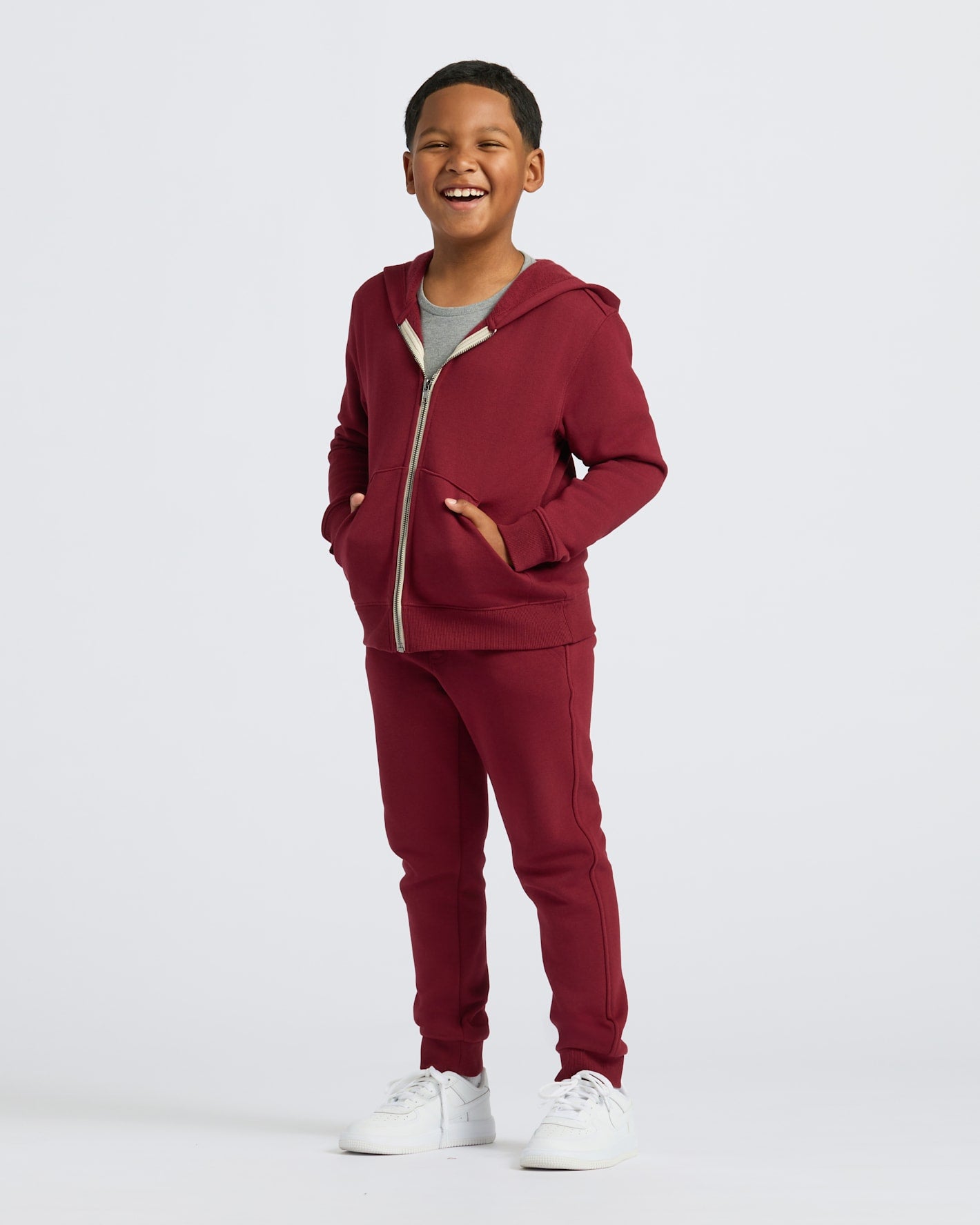 Boy in Boys' Dark Maroon Fleece Jogger, smiling with hands in pockets.