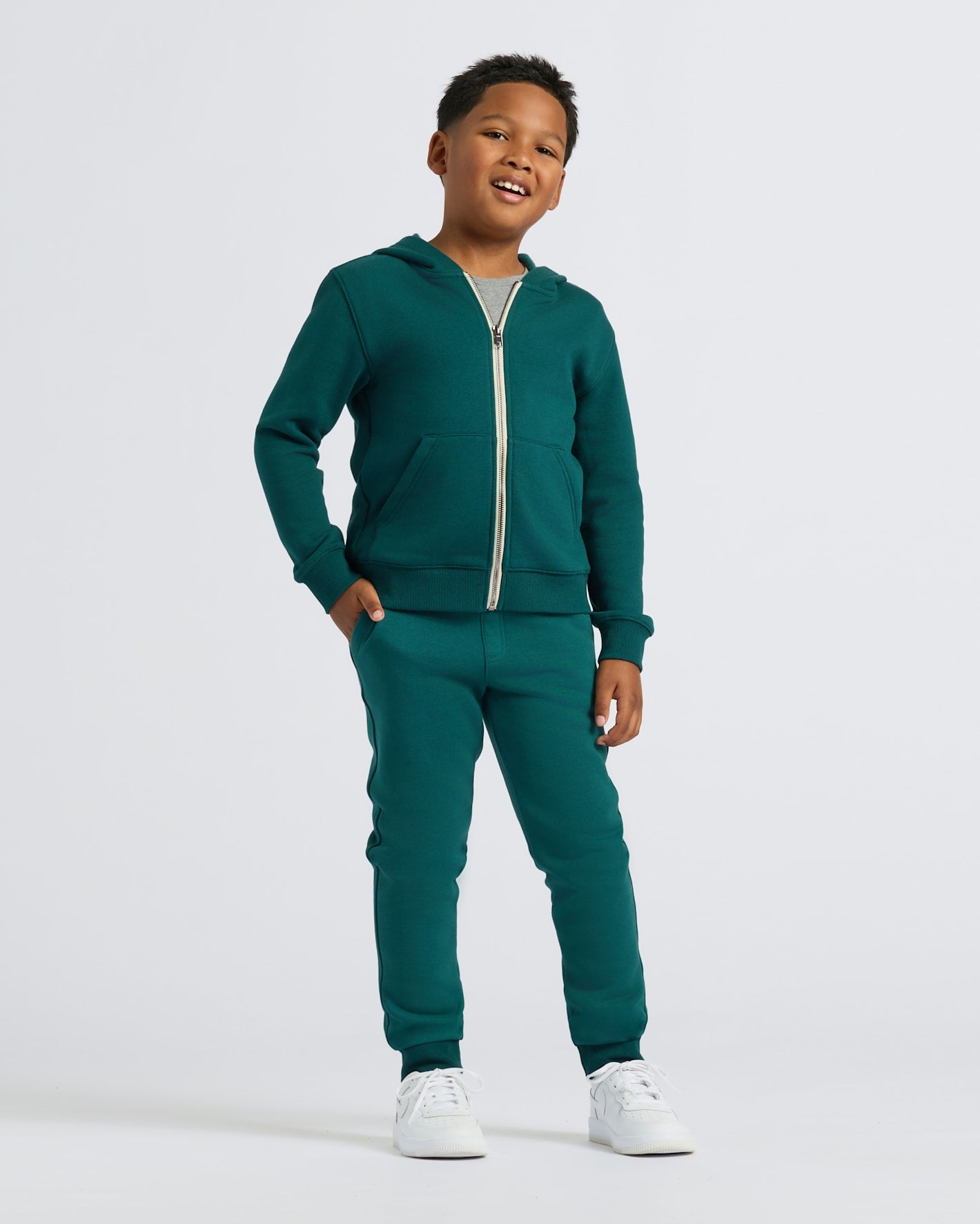 Boy wearing Boys' Deep Emerald Fleece Jogger with a zip-up hoodie, smiling.