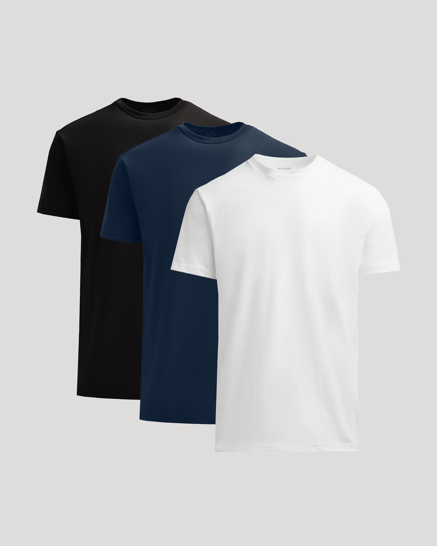 Three plain t-shirts in black, navy, and white on a light gray background