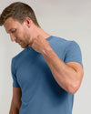 A man wearing a blue short-sleeve crewneck t-shirt, shown from the chest up against a light gray studio background.