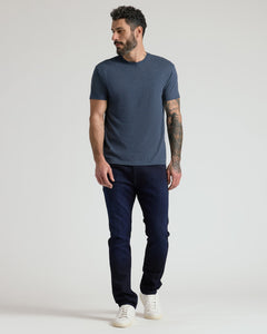 True ClassicA man wearing a heathered slate blue crewneck t-shirt, dark navy blue jeans, and white sneakers, standing against a light gray studio background.
