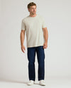 Man wearing a beige t-shirt and dark blue jeans on a white background