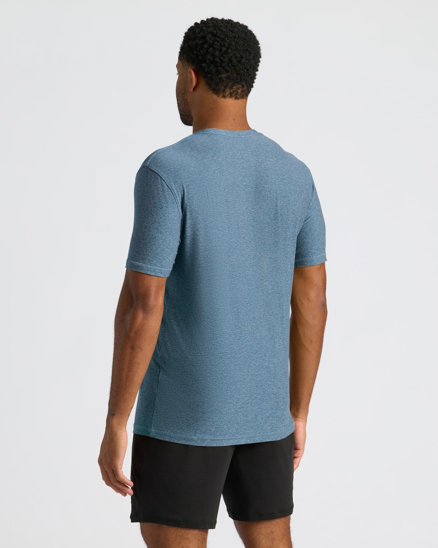 Man wearing a blue Baltic Active Crew Neck Tee standing with back facing the camera, paired with black shorts against a plain light background.