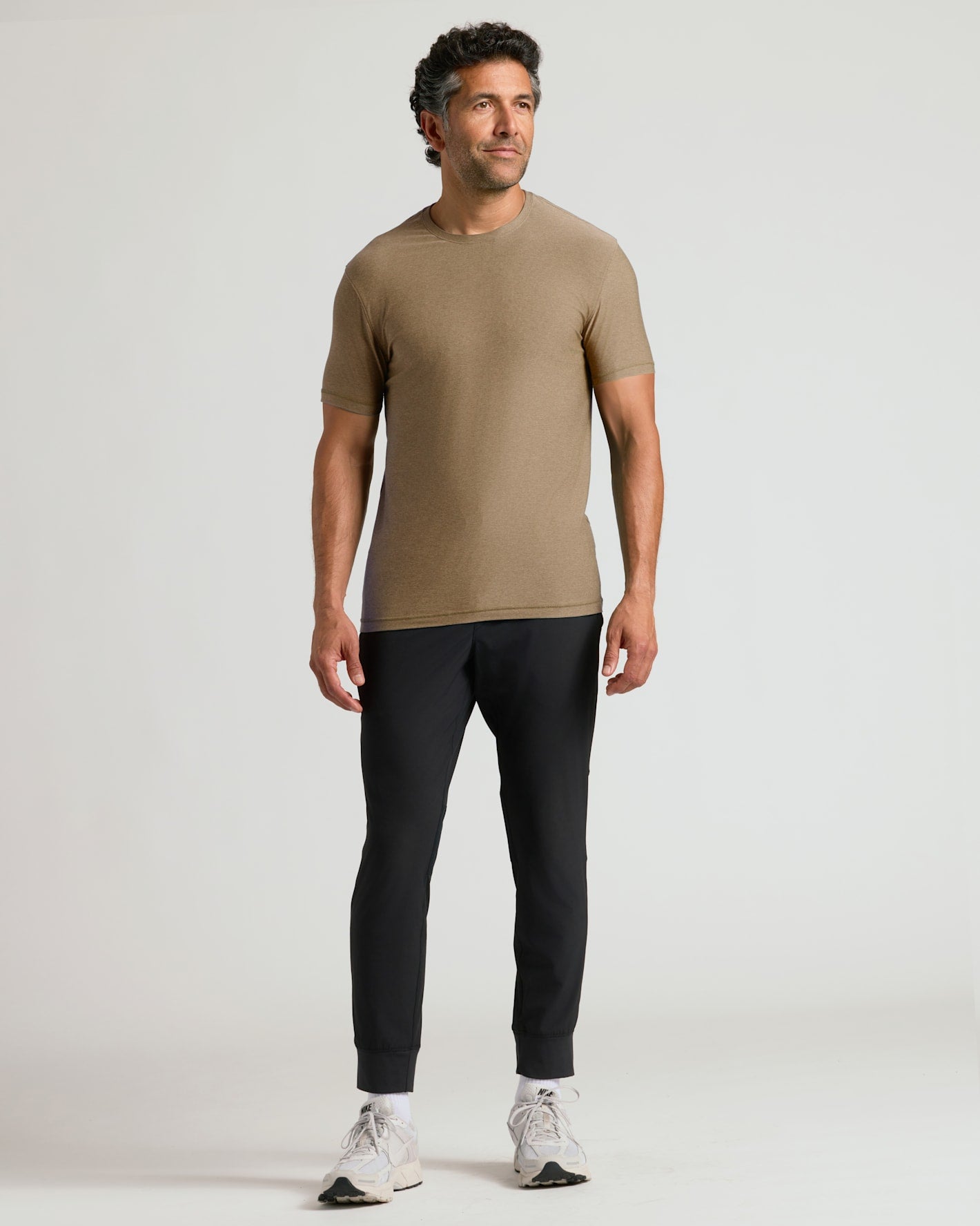 Man wearing a Driftwood Active Crew Neck Tee paired with black jogger pants and white sneakers, standing against a plain light background with a relaxed posture.
