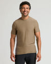 Man wearing a fitted Driftwood Active Crew Neck Tee in a neutral brown shade paired with black shorts, smiling confidently against a plain background.