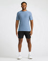 A man modeling a light blue short-sleeve athletic t-shirt and black athletic shorts against a light gray studio background.
