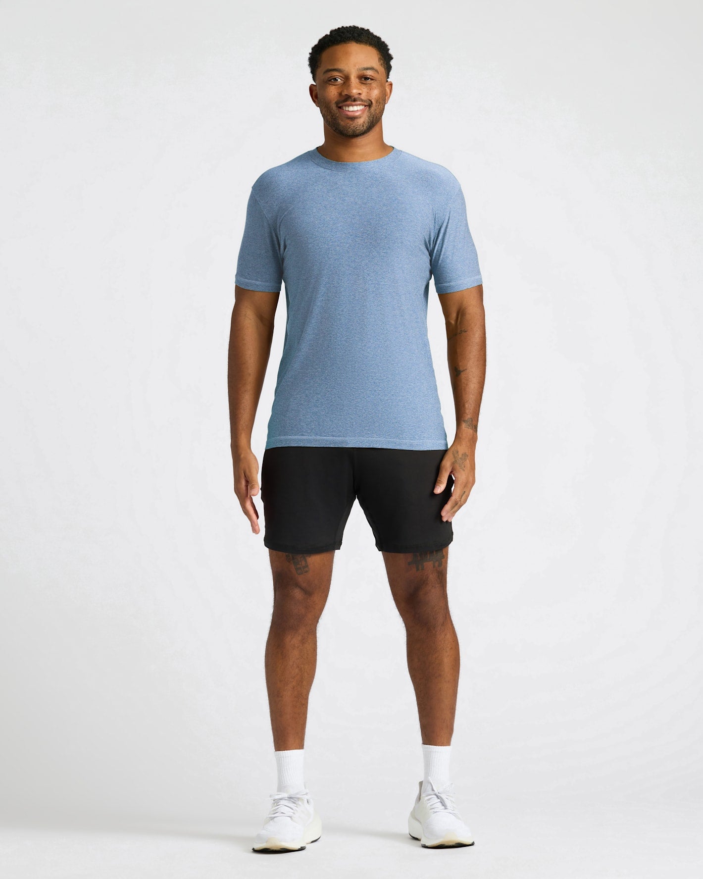 A man modeling a light blue short-sleeve athletic t-shirt and black athletic shorts against a light gray studio background.