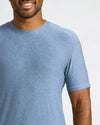 A close-up of a man wearing a heathered blue crew-neck t-shirt against a light gray background.