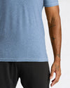 Close-up of a person wearing a heathered blue short-sleeve athletic shirt and black shorts against a light gray background.