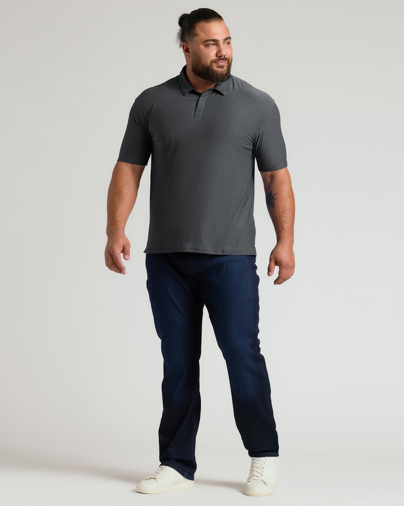 A confident man modeling a charcoal heather gray short-sleeve polo paired with dark jeans and white sneakers, showcasing the Charcoal Heather Gray Active Polo 2.0 in a casual stance.