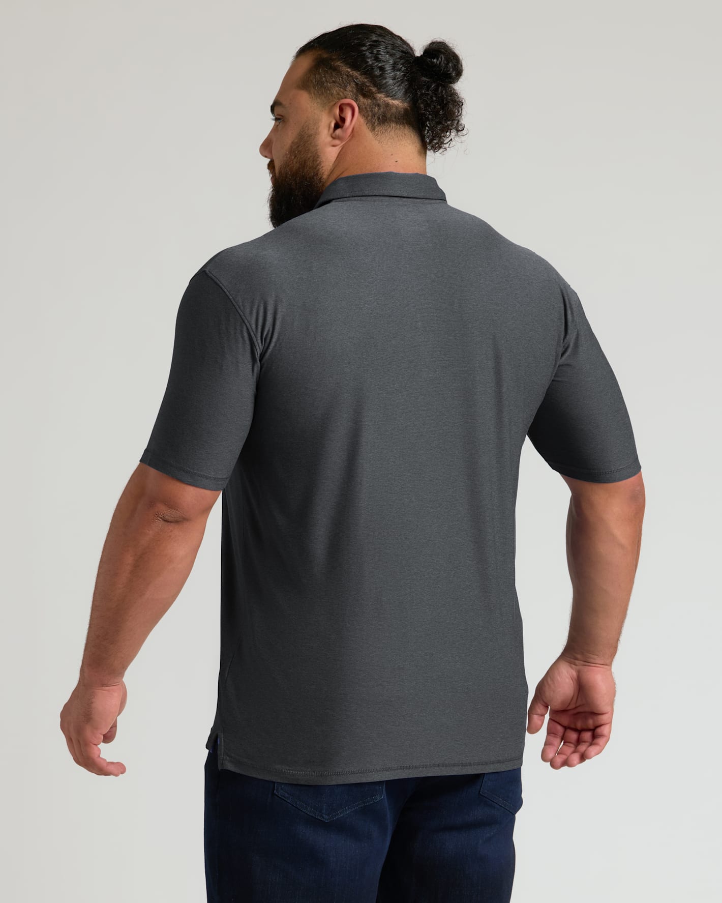 Man wearing a charcoal heather gray active polo 2.0 with short sleeves, shown from the back, paired with dark blue jeans in a studio setting