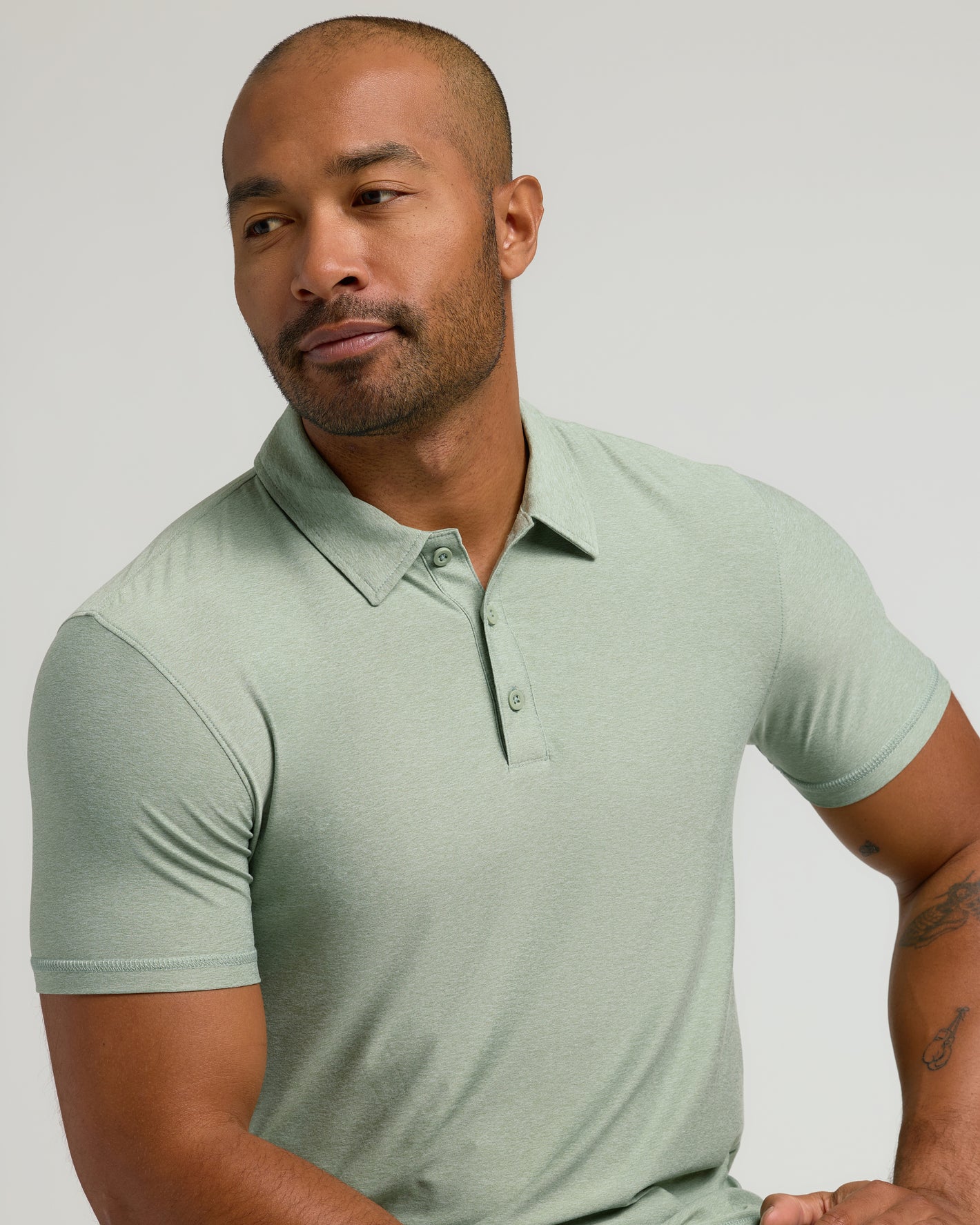 Man wearing Lichen Active Polo 2.0 with tattoos visible on forearm.