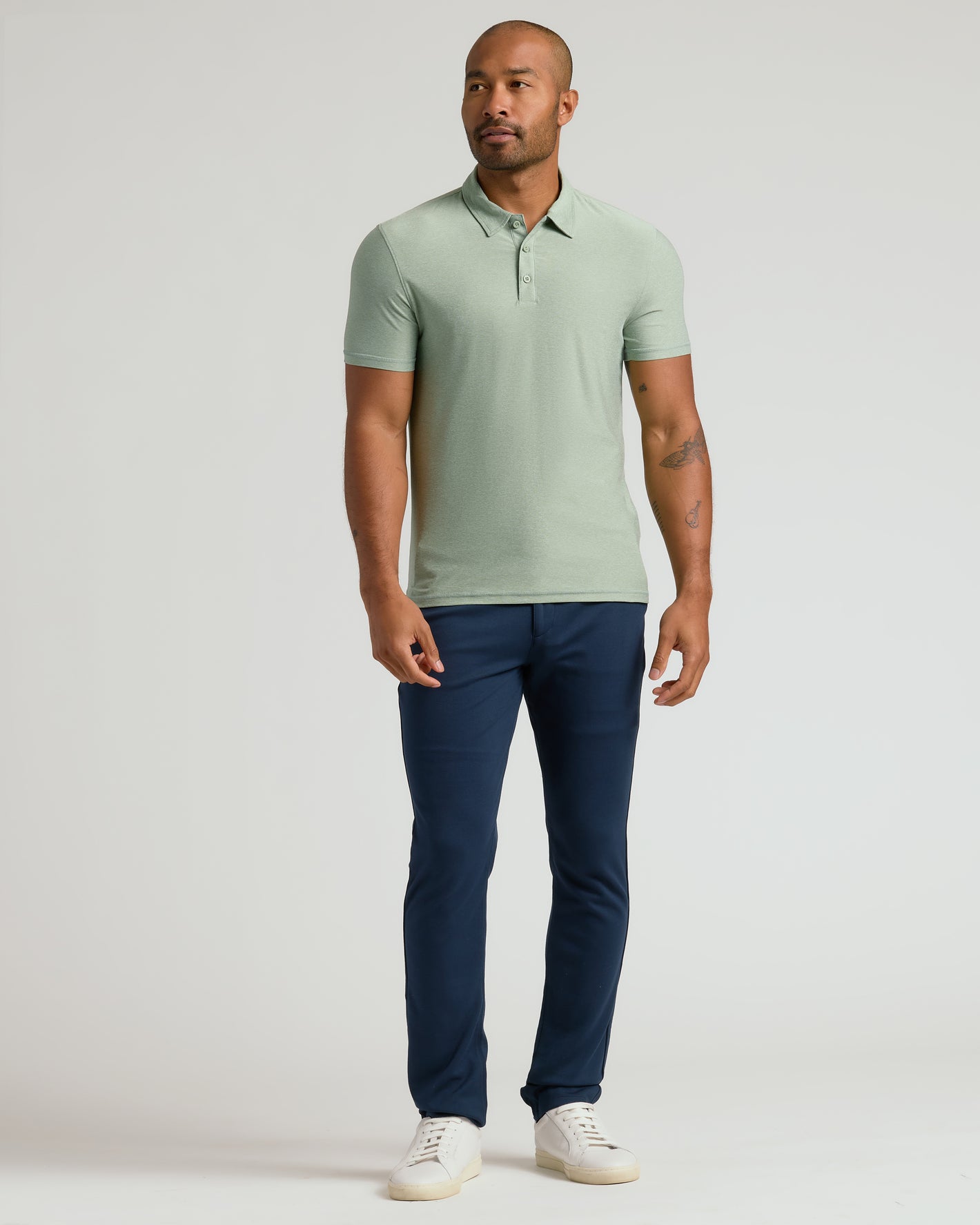 Model in Lichen Active Polo 2.0 with navy trousers, white sneakers.