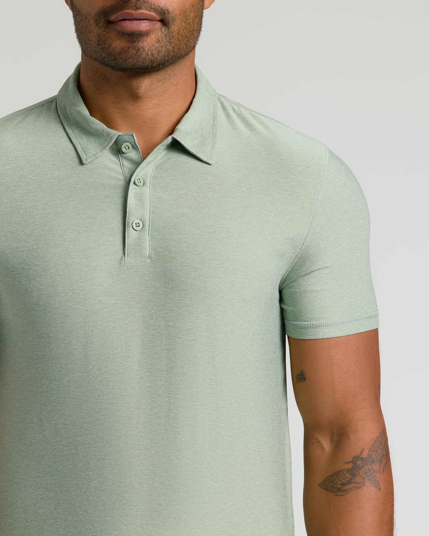 Man wearing Lichen Active Polo 2.0 with tattoos visible.