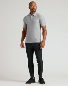 True ClassicMan wearing a Light Heather Gray Active Polo 2.0 with short sleeves, paired with black pants and black sneakers, standing against a plain light background.