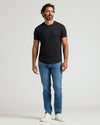 A man wearing a black Pima Cotton Blend Curved Hem Crew 4-Pack shirt paired with blue jeans and white sneakers, standing against a plain light background.