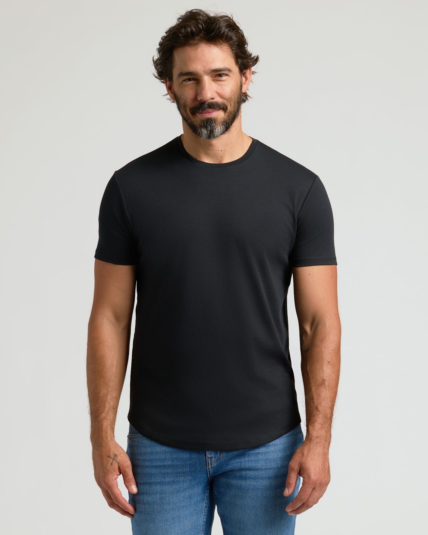 A man wearing a black Pima Cotton Blend Curved Hem Crew 4-Pack t-shirt paired with blue jeans, standing against a plain light background.